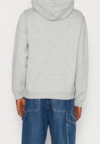 Sudadera gris con capucha y cordón, con un ajuste holgado. Combinada con pantalones cargo de mezclilla azul con bolsillos grandes y costuras visibles.