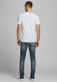 Weißes Kurzarm-T-Shirt mit Rundhalsausschnitt, kombiniert mit ausgewaschenen blauen Jeans, getragen mit weißen Schuhen. Glatte Textur, lässige Passform.