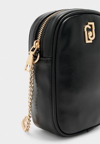 Schwarze Leder-Crossbody-Tasche mit abgerundeten Kanten, goldenen Reißverschlussbeschlägen und einem dekorativen goldenen Logo. Mit einem Ketten-Reißverschluss-Zieher.