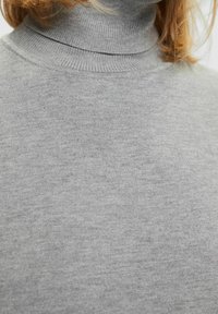 Pull à col roulé gris avec une texture côtelée douce. Présente une coupe ajustée avec un col montant et peu de détails. Convient pour être porté en superposition.