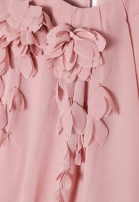 Rosa Stoffbekleidung, geschmückt mit schichtartigen, blütenblattartigen Verzierungen, die kleine goldene Akzente und eine weiche, strukturierte Oberfläche aufweisen.