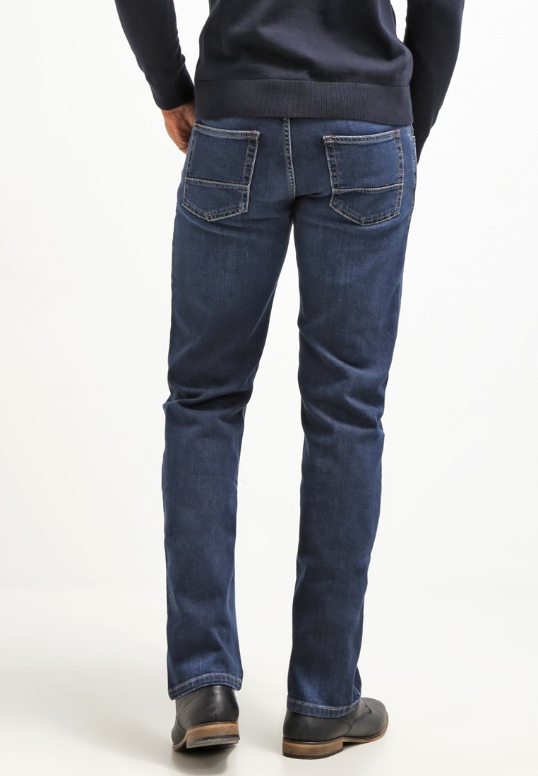 Dunkelblaue Jeans im Slim-Fit, mit zwei Gesäßtaschen, dezenter Naht und abgewetzten Kanten am Saum. Kombiniert mit schwarzen Lederstiefeln.