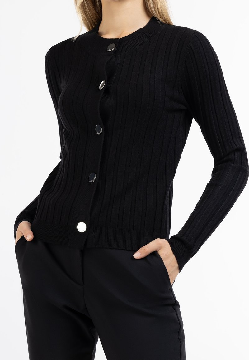 Svart rippad cardigan med rund halsringning, långa ärmar och metallknappstängning framtill. Slät stickad struktur.