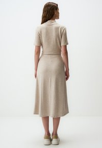 Robe tricot beige à manches courtes, col montant, et jupe fluide de longueur moyenne. Texture lisse et motif subtil avec un détail de couture au dos.