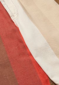 Bavlnená látka s horizontálnymi pruhmi v odtieňoch červenej, béžovej a hnedej. Textúra je hladká, s jemným leskom a viditeľným stehom.