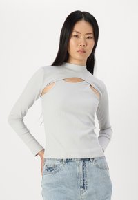 Top lungi cu dungi gri deschis, cu detalii decupate, guler înalt și textură moale, asortate cu pantaloni scurți din denim albastru cu talie înaltă.