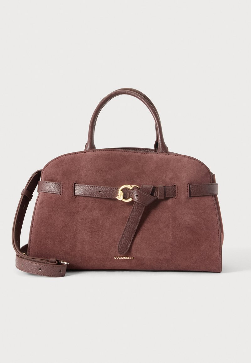 Sac à main en daim marron avec poignées en cuir, bandoulière réglable, détail boucle dorée et petit logo « COCCINELLE » sur le devant.