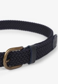Cinturón de tela trenzada en color navy con hebilla de bronce y acentos de cuero. Presenta un diseño texturizado y un detalle del logo en la pieza de cuero.