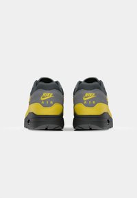 Nike Air sneakers feature a grey upper with yellow accents, a textured finish, and a black rubber sole. Logo is displayed on the heel.