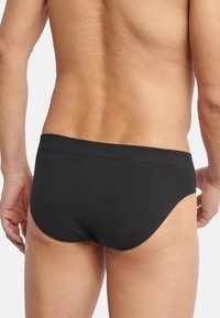 Slip in cotone nero con una cintura elastica liscia. Il design è minimale con una vestibilità aderente, che esalta la forma del corpo.