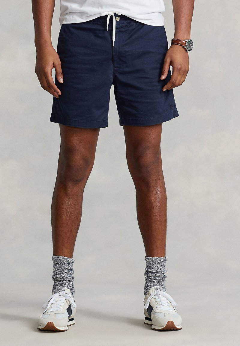 Mörkblå shorts i lätt tyg med dragsko i midjan, sidofickor och avslappnad passform, kombinerade med vita sneakers och mönstrade strumpor.