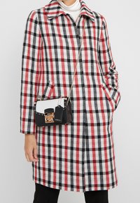 Cappotto in misto lana con motivo a quadri nero, bianco e rosso, maniche lunghe e colletto con risvolto; abbinato a una piccola borsa a tracolla bianca e nera.