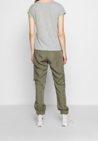 Grå kortærmet t-shirt parret med olivengrønne cargo-bukser med sidelommer og elastiske manchetter, iført hvide høj-top sneakers.
