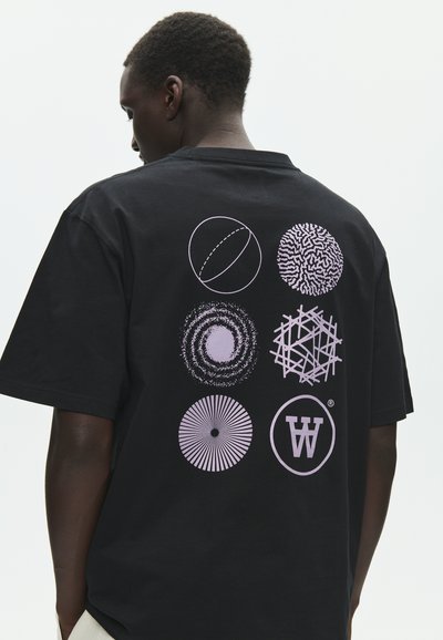 Άτομο με μαύρο T-shirt που κοιτάζει προς τα πίσω, με έξι διακριτά κυκλικά σχέδια σε ανοιχτό μοβ χρώμα στην πλάτη.