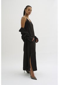 Svart satin klänning med djup V-ringning och hög slits, tillsammans med en oversized svart jacka som har knapppdetaljer och textilstruktur.