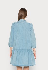 Ljusblå denimklänning med trekvarts puffärmar, ett lager på lager volangnederkant och en knapp-up krage. Slät textur, avslappnad design.