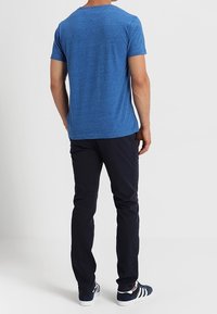 Blå hede kortärmad t-shirt i mjukt tyg, matchad med navy-byxor och sneakers med blå detaljer, sedd bakifrån.