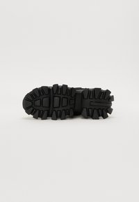 Baskets noires avec une semelle robuste et texturée dotée de profonds crampons. La partie supérieure présente des accents en maille et un design solide, adapté à une utilisation en extérieur.