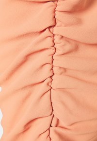 Gros plan d’un tissu couleur pêche avec des coutures froncées formant des plis texturés le long de la couture centrale.