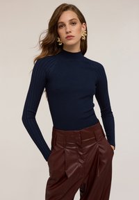 Top a collozzo navy a coste presenta un design aderente con maniche lunghe, abbinato a pantaloni bordeaux lucidi a vita alta.