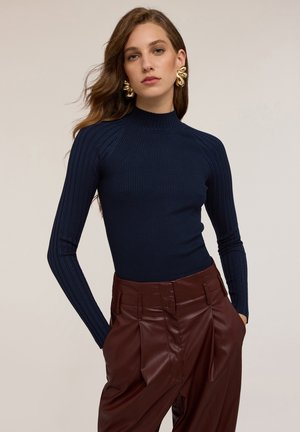 Top a collozzo navy a coste presenta un design aderente con maniche lunghe, abbinato a pantaloni bordeaux lucidi a vita alta.