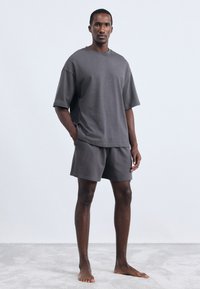 Set din bumbac gri închis, format dintricouri cu mânecă scurtă și pantaloni scurți. Cămășile au o croială lejeră și un guler rotund, în timp ce pantalonii scurți au un elastic în talie.