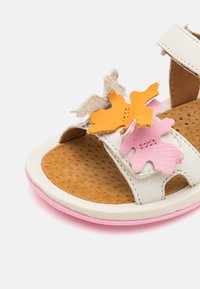 Sandalo in pelle bianca con accenti a forma di foglia colorati in giallo, rosa e beige, dotato di una soletta perforata marrone e una suola rosa.