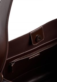 Innenraum einer dunkelbraunen Ledertasche mit Magnetverschluss und Reißverschlusstasche mit passendem Lederlasche.