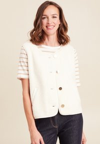 Weißer Fleece-Weste mit rundem Hals, vorderen Knöpfen und Seitentaschen. Getragen über einem creme- und beigen gestreiften Hemd.