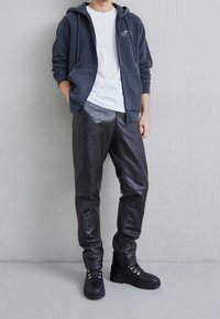 Felpa navy con tasche frontali, T-shirt bianca sotto, pantaloni neri lucidi in ecopelle con motivo coccodrillo e stivali neri con lacci.
