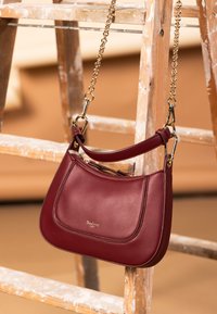 Burgundy leather handbag with a smooth texture, gold chain strap, and zip closure. Features subtle stitching and a logo detail on the front.