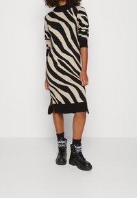 Stickad klänning med svarta och beige zebraränder, med ribbade muddar och fåll, sidoklyfta, ihop med svarta snörstövlar.