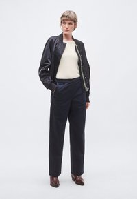 Jachetă bomber neagră, manșete striate, pulover tricotat crem, pantaloni bleumarin, textură netedă, cizme maro cu toc. Siluetă simplă, modernă.