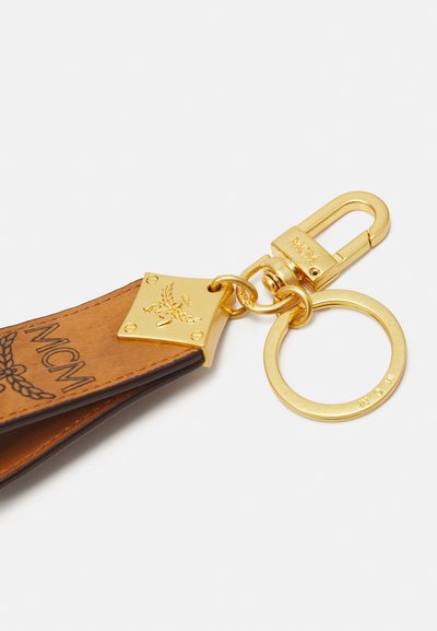 Breloc din piele cu o schemă de culori bej și maro închis, accesorii aurii, gravură și un suport circular pentru chei detașabil.