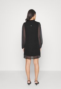 Black dress with sheer puff sleeves, textured fabric featuring small embellishments, above-knee length, with a scalloped neckline and back button.