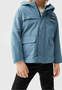 Vaaleansininen vettä hylkivä takki hupulla, vetoketjukiinnitys, kaksi etutaskua ja pieni logopatchi rinnassa. Rakennekangas.