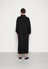 Sort, oversized, langærmet kjole med høj krave, lavet af blødt materiale, med en lige silhuet og ribbede manchetter. Bæres med sorte sneakers.