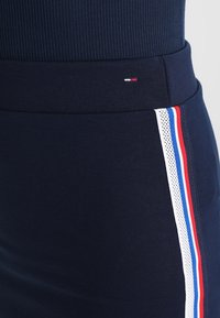 Námořnická sukně s žebrovaným pasem, přiléhavým střihem a bočními pruhy v červené, bílé a modré barvě s detaily z textilu s mírnou průhledností.