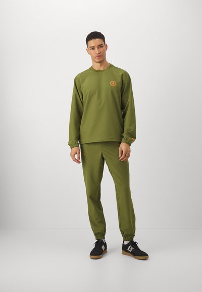 Olive green sweatshirt and matching pants made from soft fabric. Features elastic cuffs and a small orange logo on the chest and pant.