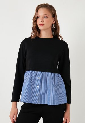 Black long-sleeve top with a blue and white striped peplum section, featuring button accents at the front. Soft fabric texture throughout.