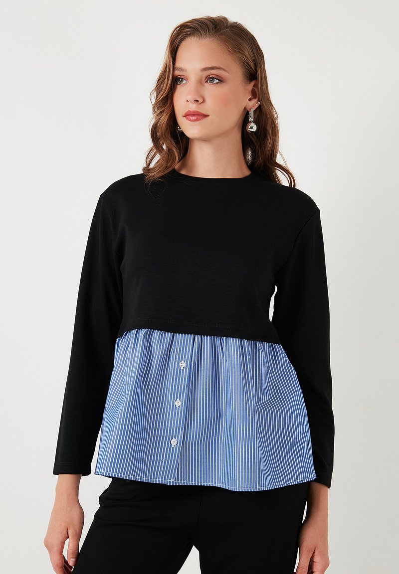 Top nero a maniche lunghe con una sezione peplum a righe blu e bianche, con dettagli a bottoni davanti. Tessuto morbido in tutto il capo.