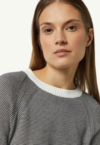 Schwarz-weiß gestreifter Strickpullover mit einem gerippten weißen Kragen und Raglanärmeln, der ein strukturiertes Muster und eine enganliegende Passform aufweist.