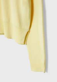 Pull en tricot jaune avec une texture douce. Il présente un col rond, des manches longues et des poignets côtelés. Aucun motif ni élément métallique visible.