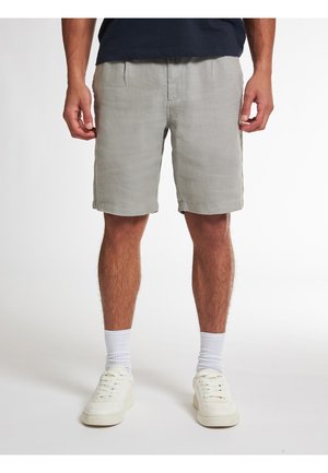 Hellgraue Leinen-Shorts mit einem lockeren Schnitt, mit Seitentaschen und umgeschlagenem Saum. Kombiniert mit weißen Turnschuhen und Socken in Knöchelhöhe.