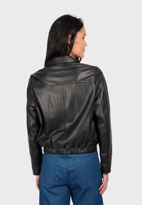 Černá kožená bunda s límcem, zkráceným střihem a elastickým pasem. Má hladký povrch a jemné švy.