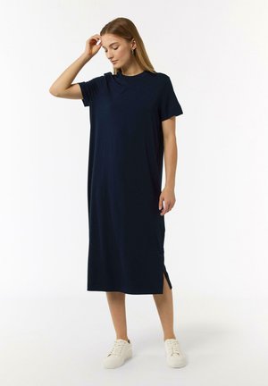 Marineblaues, knielanges Kleid mit kurzen Ärmeln, seitlichen Schlitzen und lockerer Passform. Aus weichem Stoff mit glatter Textur. Weiße Sneakers.