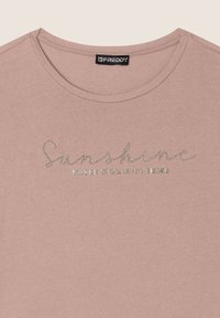 Camiseta de algodón rosa claro con cuello redondeado, que presenta un brillo plateado en el texto que dice "La luz del sol hace brillar tu alma."