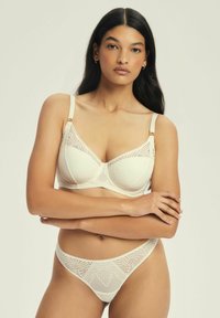 Cream lace bra and matching thong with floral patterns, delicate straps, and textured fabric. The design features a triangle shape for the cups.
