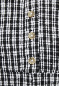 Svart och vit rutigt tyg med framträdande vertikala och horisontella linjer, med tre beige knappar längs knäppningen.