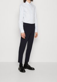 Camisa de rayas en azul claro y blanco con botones y mangas largas, combinada con pantalones ajustados azul marino y mocasines negros. Tejidos suaves y corte entallado.